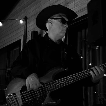 Musician in a cowboy hat playing an electric bass guitar in low light.