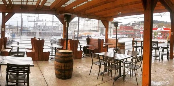 Outdoor covered seating area with wooden tables, chairs, and barrels.