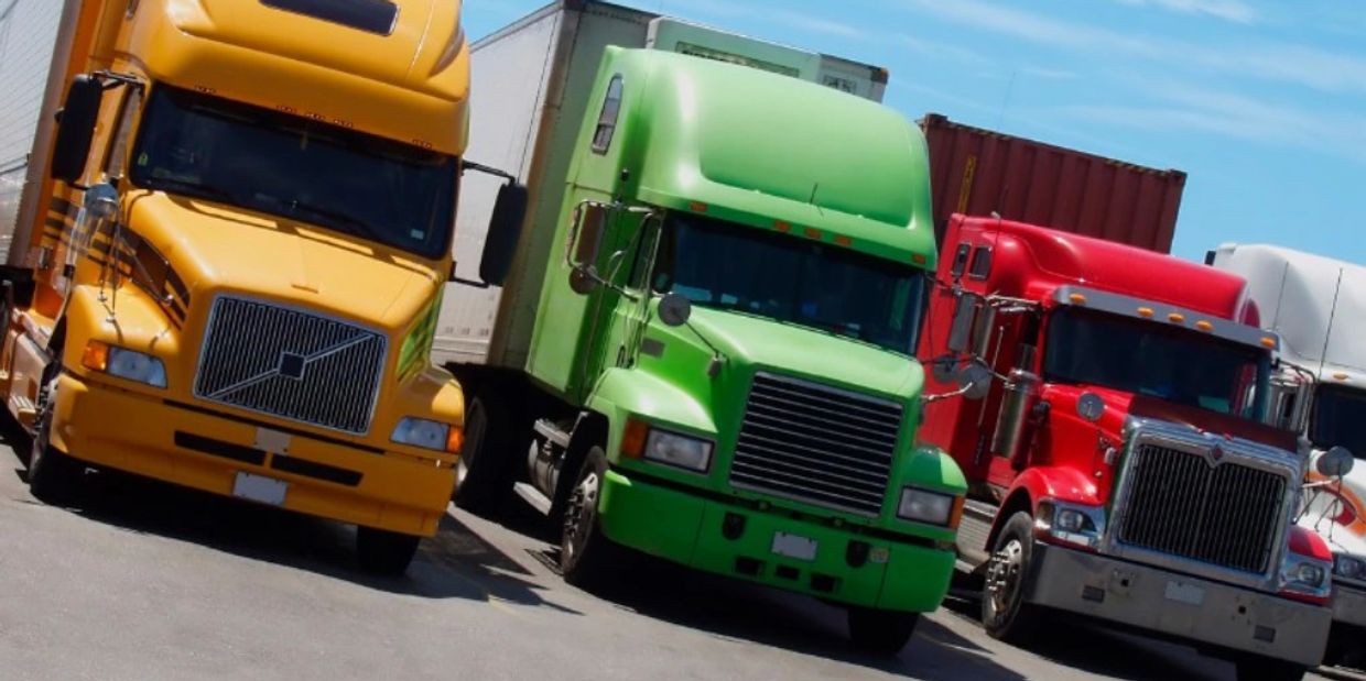 Three colorful semi-trucks parked side by side under a clear sky.