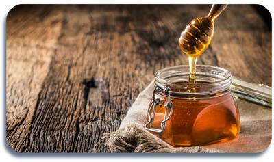Honey dripping from a wooden dipper into a glass jar on a rustic wooden table.