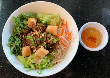 Vietnamese-style rice noodle bowl with grilled meat, fresh vegetables, spring rolls, and dipping sauce.
