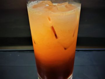 A glass of iced Thai tea with milk, showing distinct layers.
