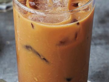 A glass of iced milk tea with ice cubes and a spoon on a marble surface.