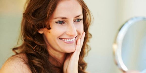 Happy, middle aged woman looking into a hand held mirror,
