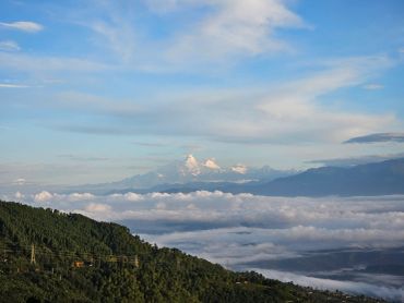 Snow-capped mountains rise above a sea of clouds under a blue sky.
