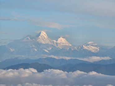 Snow-capped mountains towering above a sea of clouds under a clear sky.