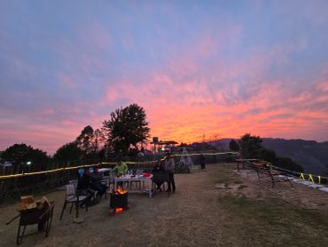 People enjoying a bonfire at sunset with a vibrant sky.