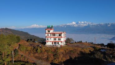A white house on a hill with snowy mountains in the background under a clear blue sky.