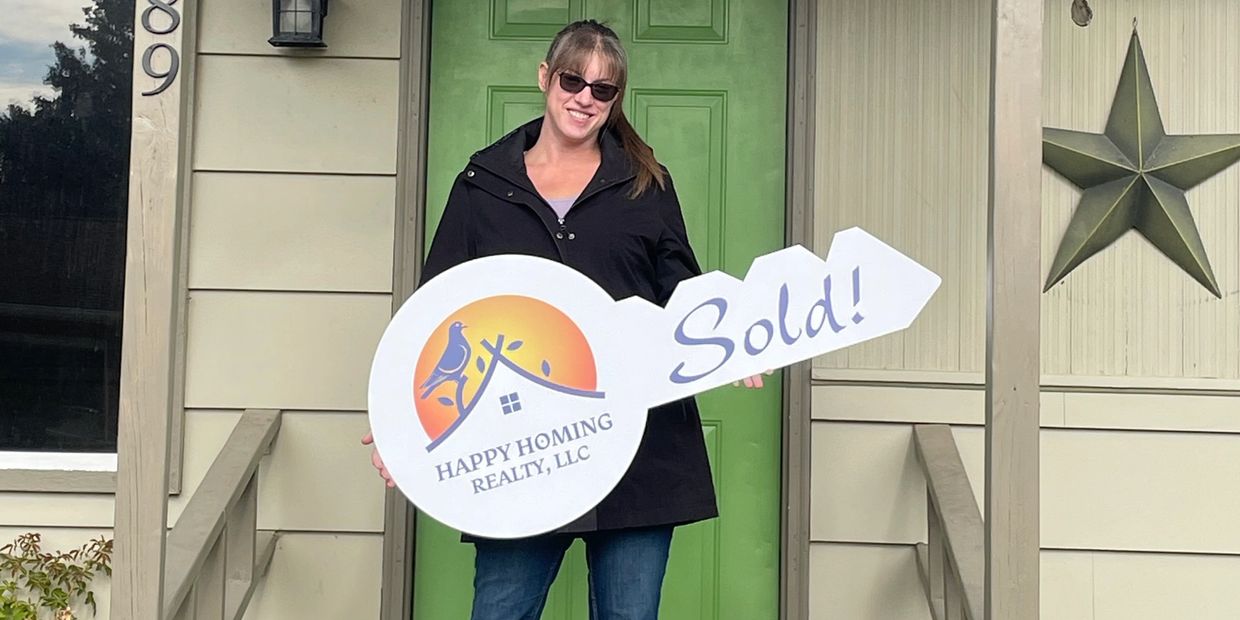 Woman standing in front of a house holding a large key sign that says "Sold!"