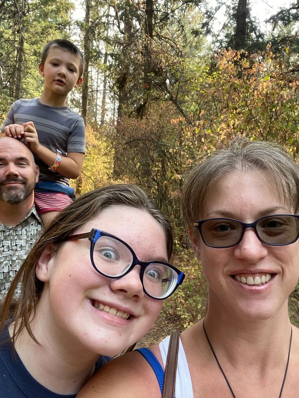 A happy family selfie outdoors with trees in the background.