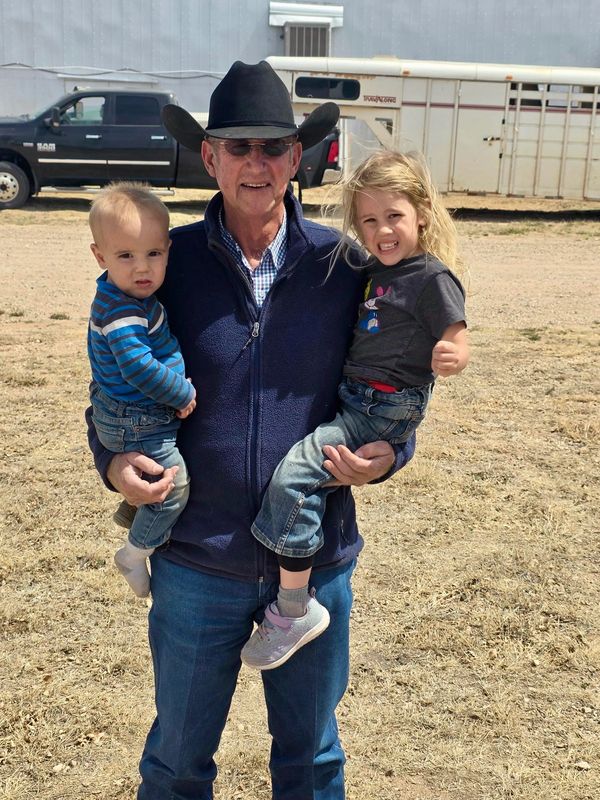 Older man in cowboy hat holding two young children outdoors.