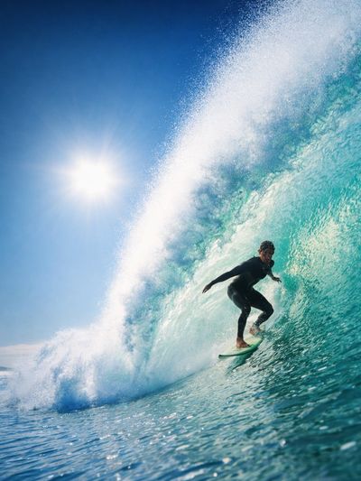 Surfer riding inside a large wave under the sun.