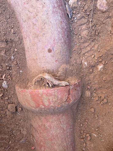 A broken red clay pipe partially buried in dirt.