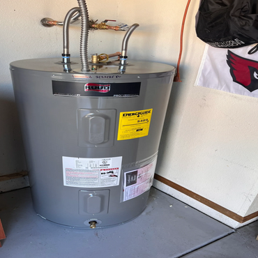 A gray RUUD water heater installed in a garage corner with energy guide label.