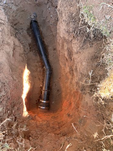 Black drainage pipe installed in a dug trench with exposed soil and grass edges.