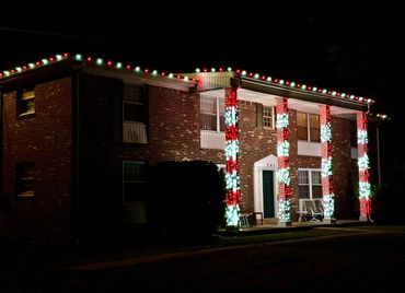 A brick house decorated with red and white Christmas lights on columns and roof edges at night.