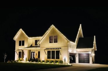 Modern house outlined with warm white Christmas lights at night.