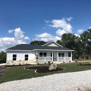 A modern single-story house with white exterior and front porch under a blue sky.