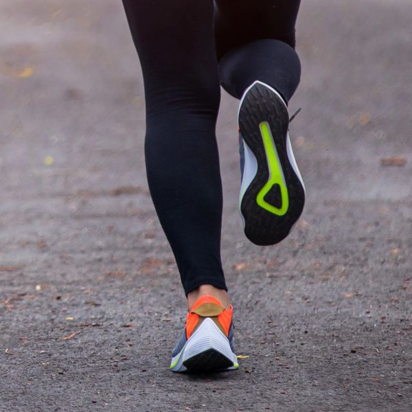 Person running on a path wearing black leggings and colorful shoes.