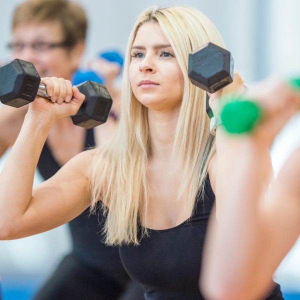 Woman lifting dumbbells in group fitness class.
