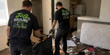 Two workers cleaning a messy room filled with trash.