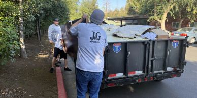 Two men loading debris into a dumpster on a sunny day.