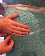 hands on pregnant belly while measuring with ribbon. Woman is wearing a blue dress with lace design