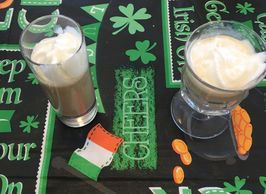 Two drink glasses with brown liqueur and white cream on top on a St. Patrick's Day tablecloth