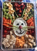 Bunny face of fruit, vegetables and cheese appetizers. arranged around a bread bowl with dip