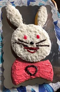 Cake cut and decorated like a bunny face, covered in white frosting and coconut