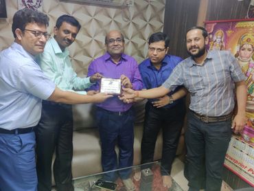 Five men holding a plaque together, standing indoors.