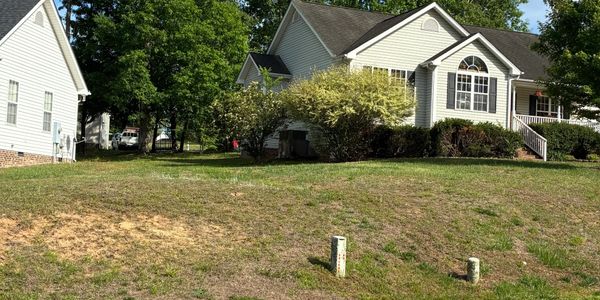 Front yard of a suburban house with patchy grass and bushes.