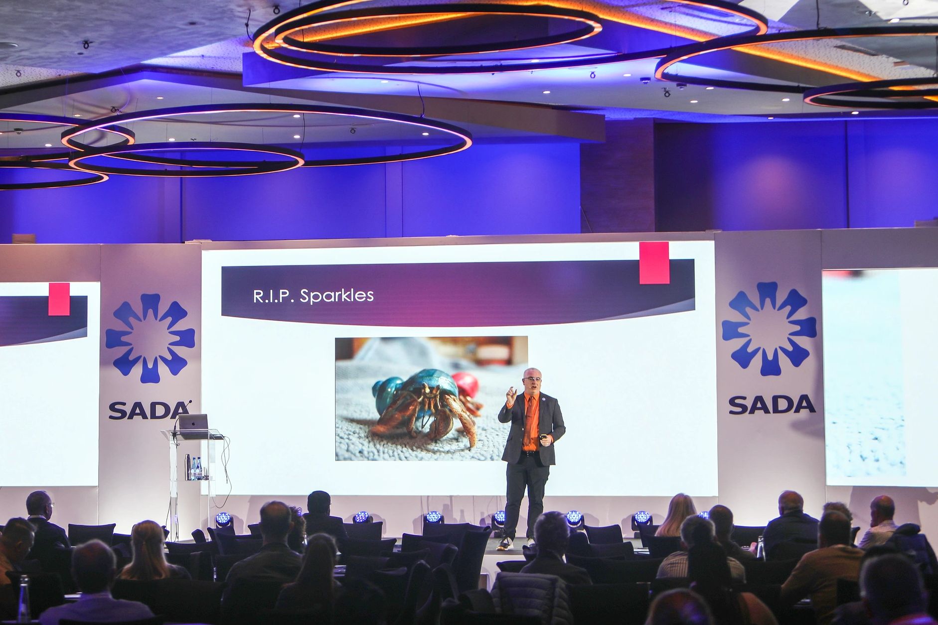 A speaker presents at a SADA event with a slide titled 'R.I.P. Sparkles'.