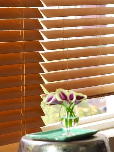 Stained wood window blinds with visible route holes installed in a residential window