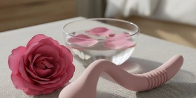 Pink silicone curved object next to a pink rose and a bowl with floating petals.