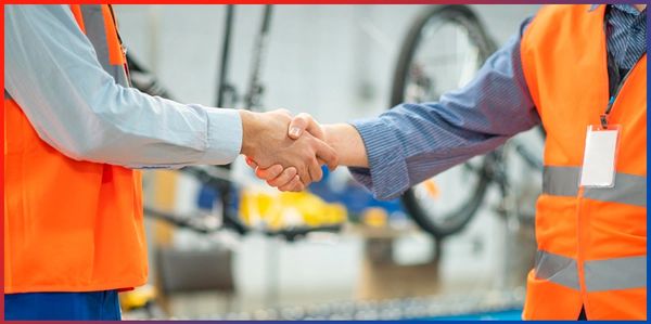 Two workers shaking hands in a factory.
