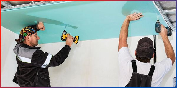 Two workers installing a ceiling panel.