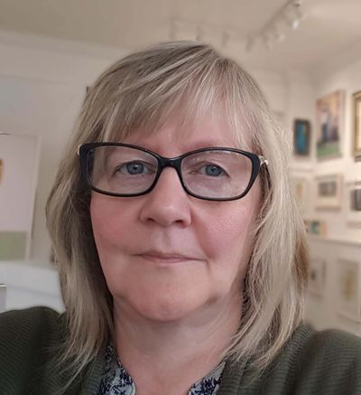 Middle-aged woman with glasses and blonde hair in an art gallery.