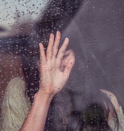 A woman behind a rainy window is in distress.