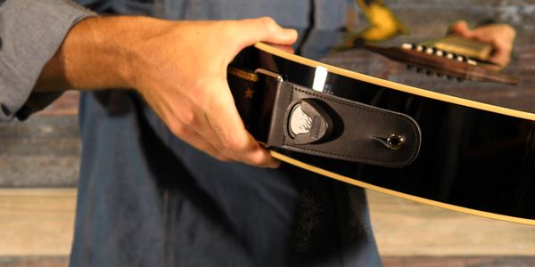Person tuning a black acoustic guitar.