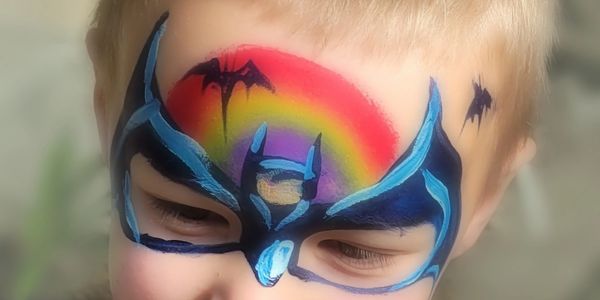 Smiling boy with a rainbow over a batman mask with bats.