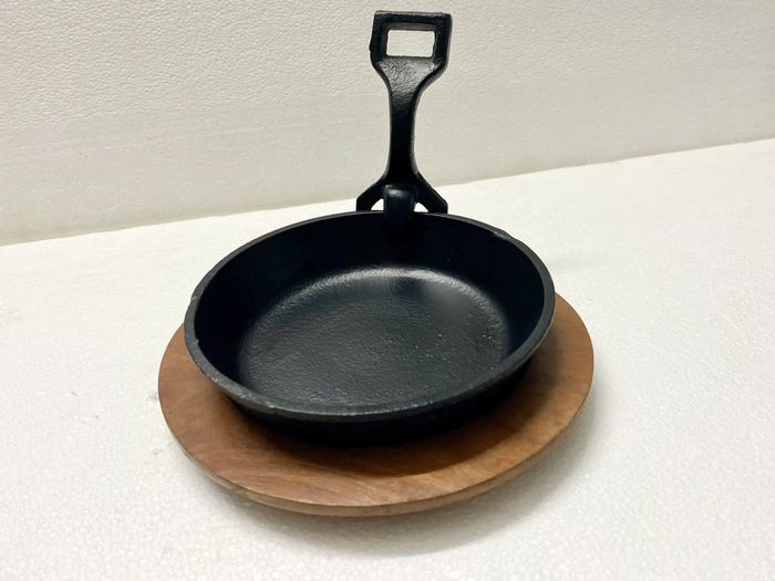 Small cast iron skillet with a wooden base on a white surface.