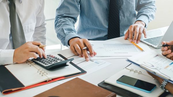 Financial professionals collaborate at a desk, reviewing charts and data with a calculator and pens