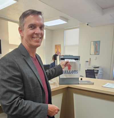 Smiling man casts his ballot at a voting station indoors.