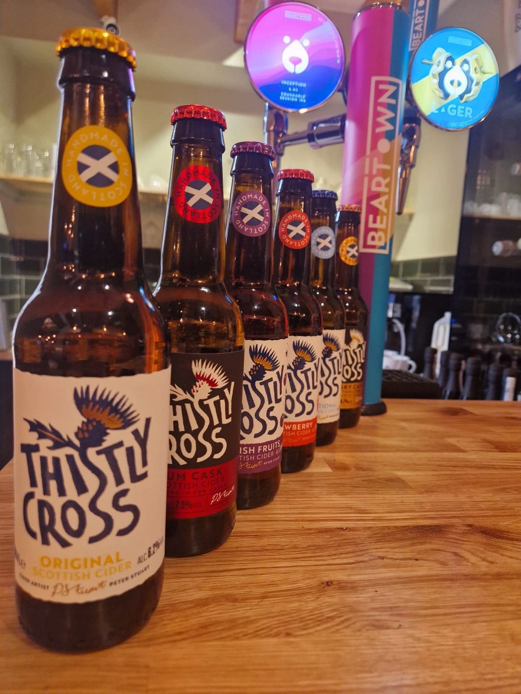 Various Thistly Cross Scottish cider bottles lined up on a wooden bar counter.