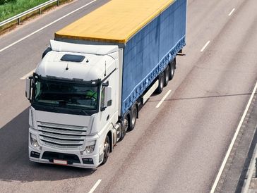White semi-truck with blue and yellow trailer on highway.