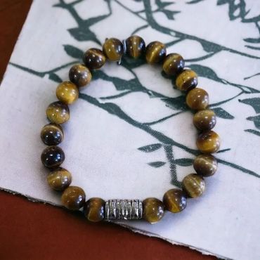 Bracelet with polished brown and black beads on a patterned cloth.