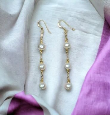 Delicate gold and pearl drop earrings on a soft fabric background.