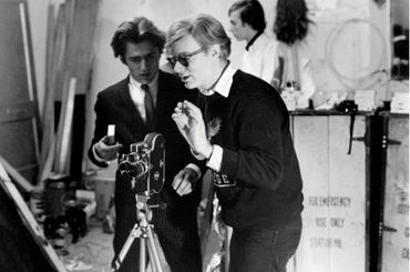 Black and white photo of Gerard Malanga and Andy Warhol setting up a movie camera.