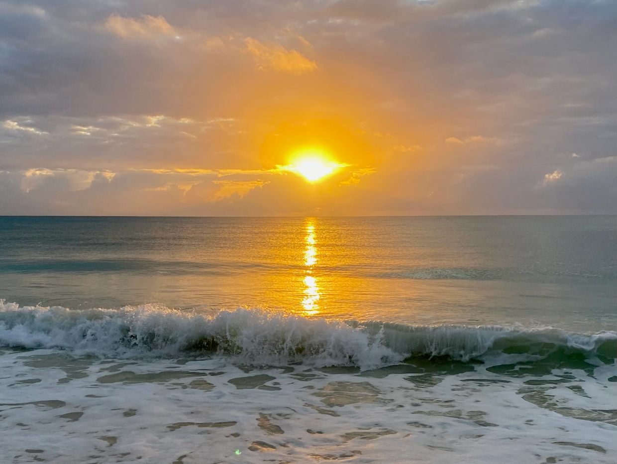 Sunset over calm ocean waves with vibrant orange reflections.